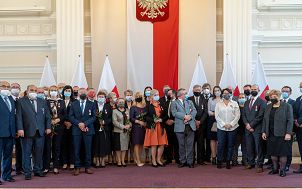 grupa odznaczonych m.in. Medalami za Długoletnią Służbę pozujących do zdjęcia na tle godła Polski oraz flag RP.